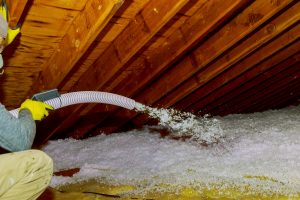 Technician spraying blown Fiberglass Insulation between Attic Trusses foam insulation construction foam from the gun to the roof