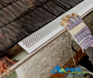 Gloved hand installing a gutter guard on a roof.