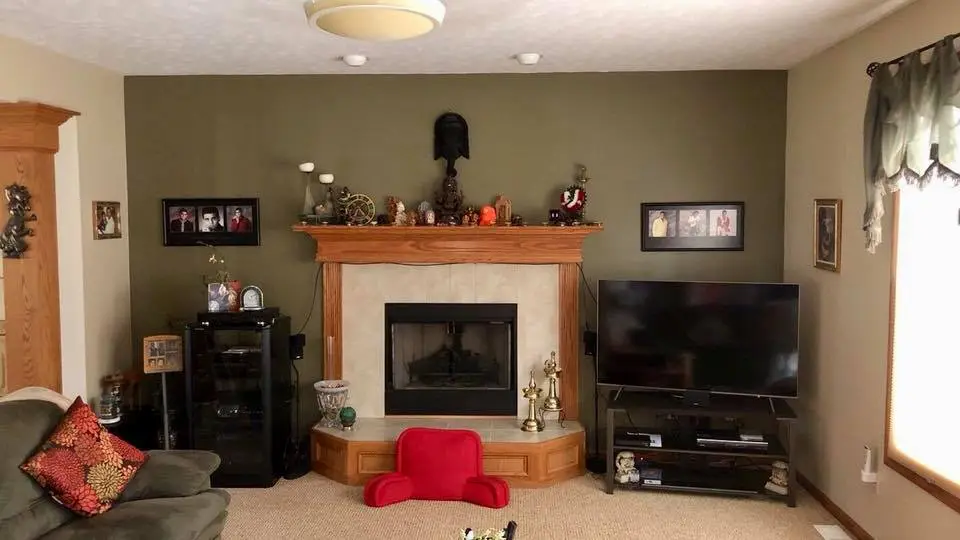 Image of interior wall of a Living room. A green wall with a fire place with a mantle centered, a tv to the right and curio cabinet to the left