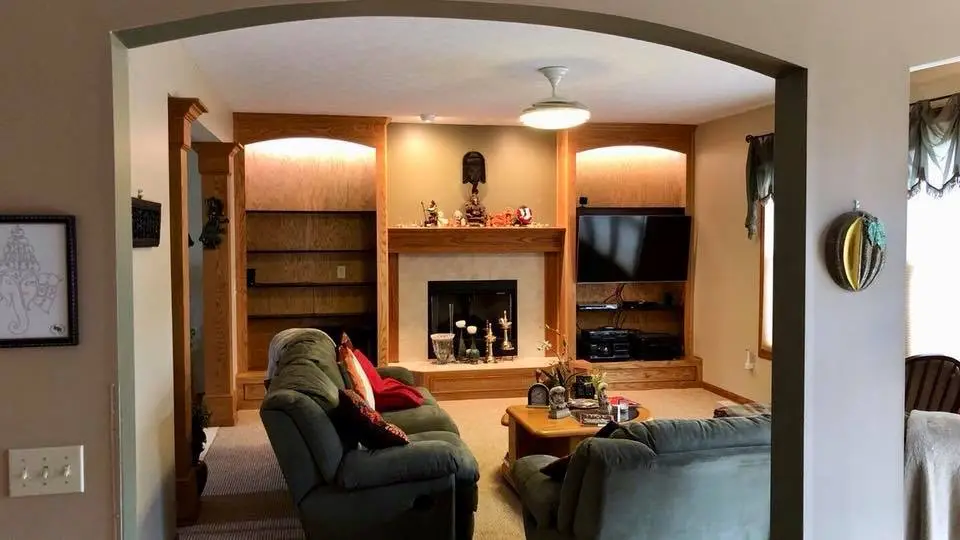 A new arch way wall opening to a living room. The far wall has a fireplace centered between 2 built-in shelves on either side.