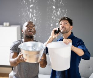 2 men holding buckets, catching water from a leaky roof.