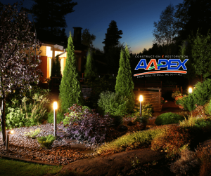 Exterior of a home at night with lighting amongst the greenery. Aapex logo top right.