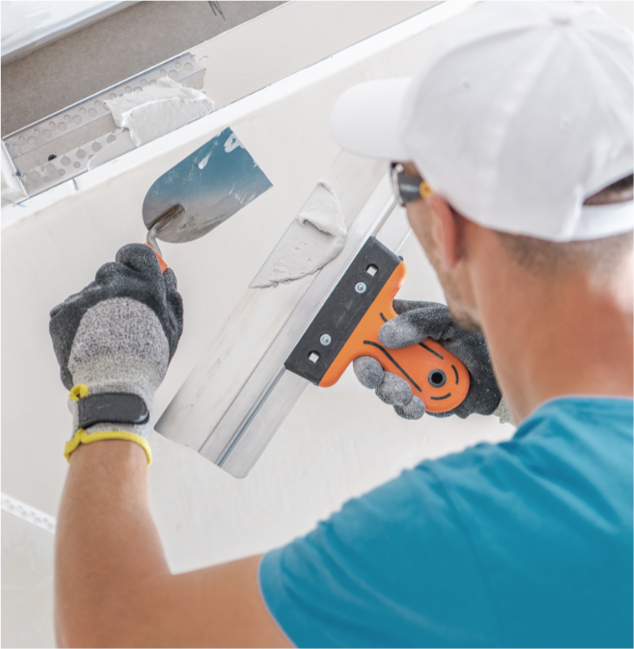 Man in a t-shirt and hat working on drywall.